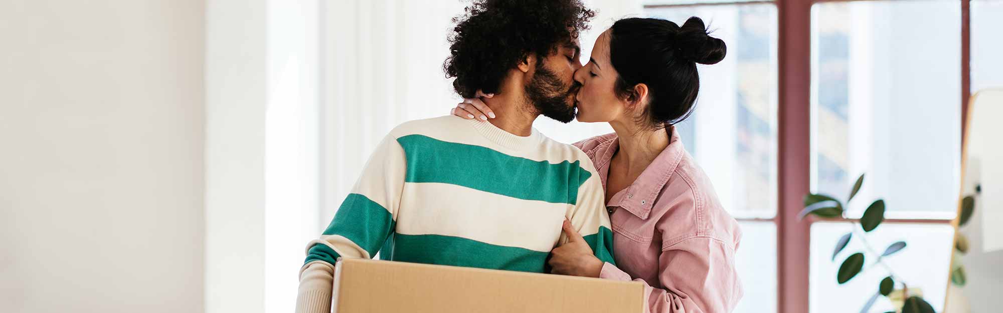 Par står i ett hus och pussas, mannen håller en flyttkartong