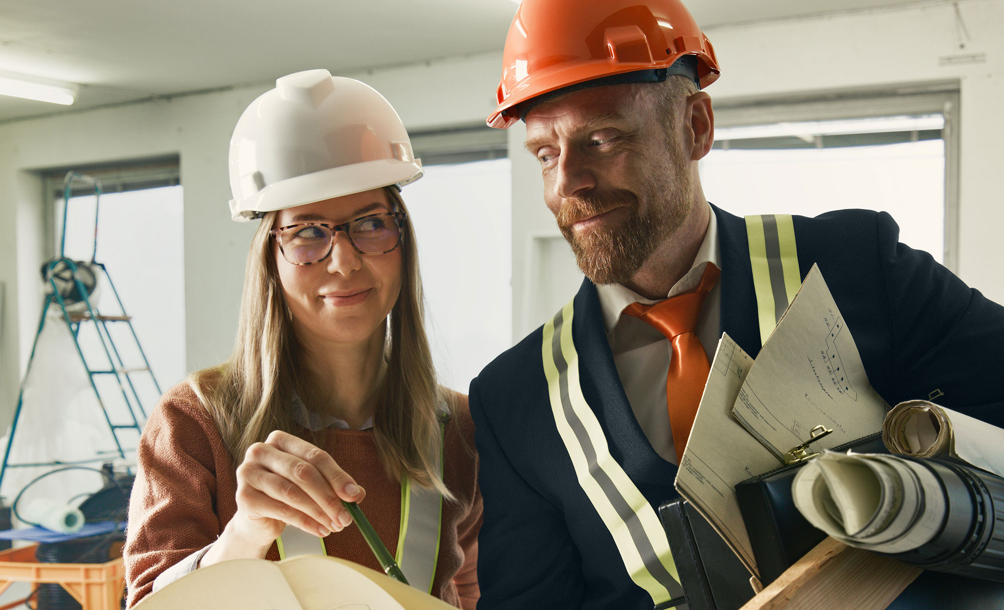 Två arkitekter diskuterar ritningar på en byggarbetsplats.