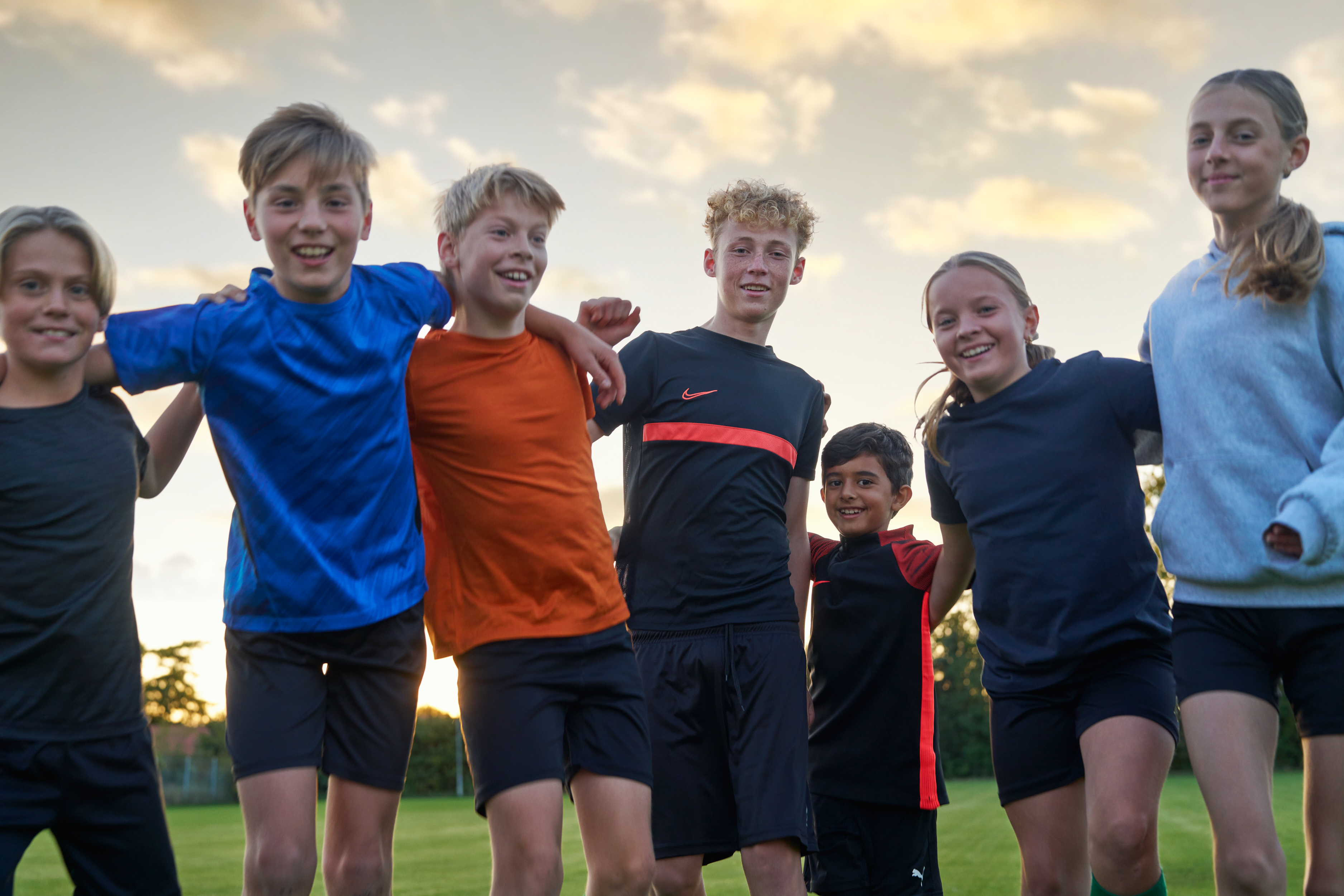 Sju barn och unga håller om varandra och ler. 