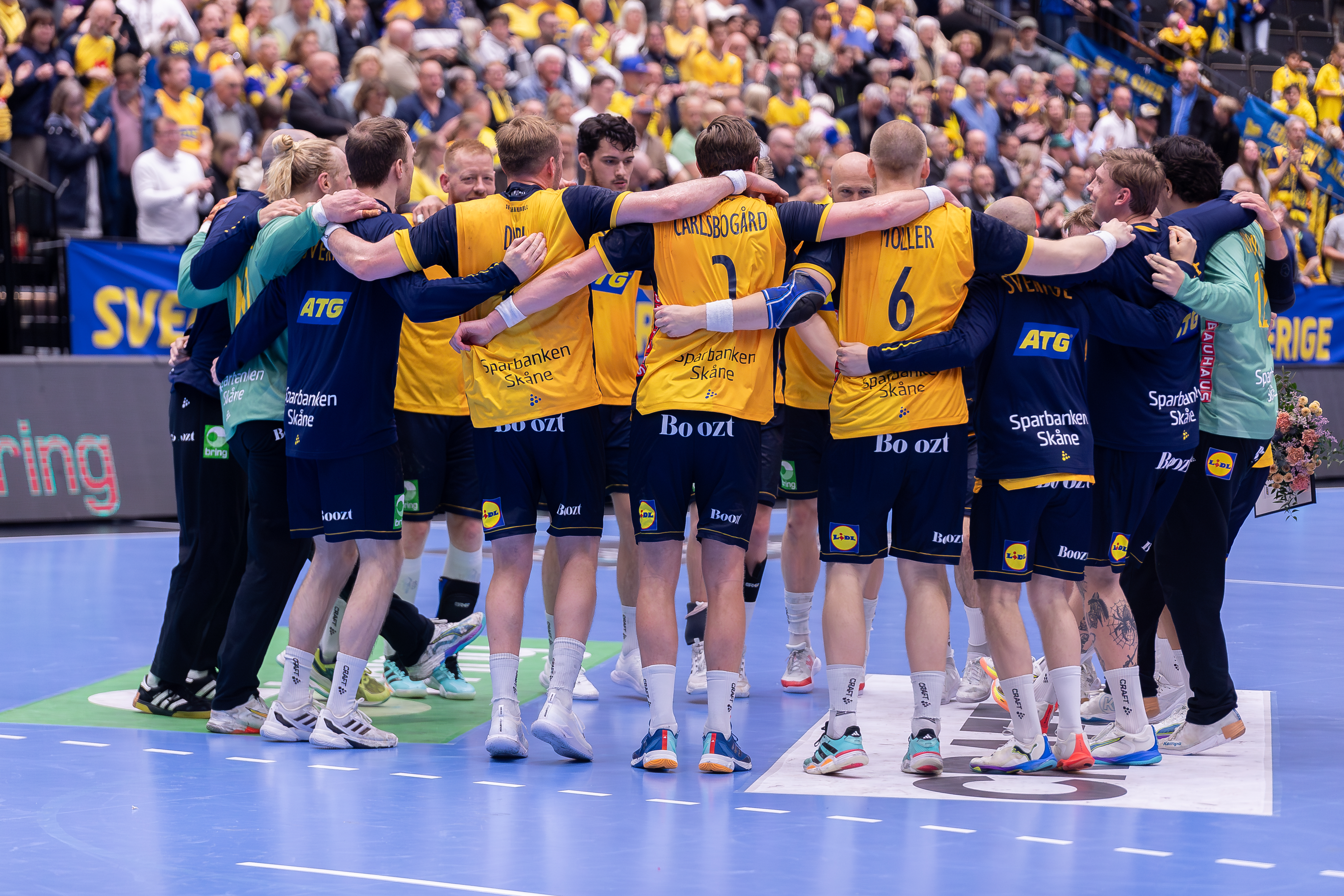 Svenska handbollslandslaget står i en ring och håller om varandra.
