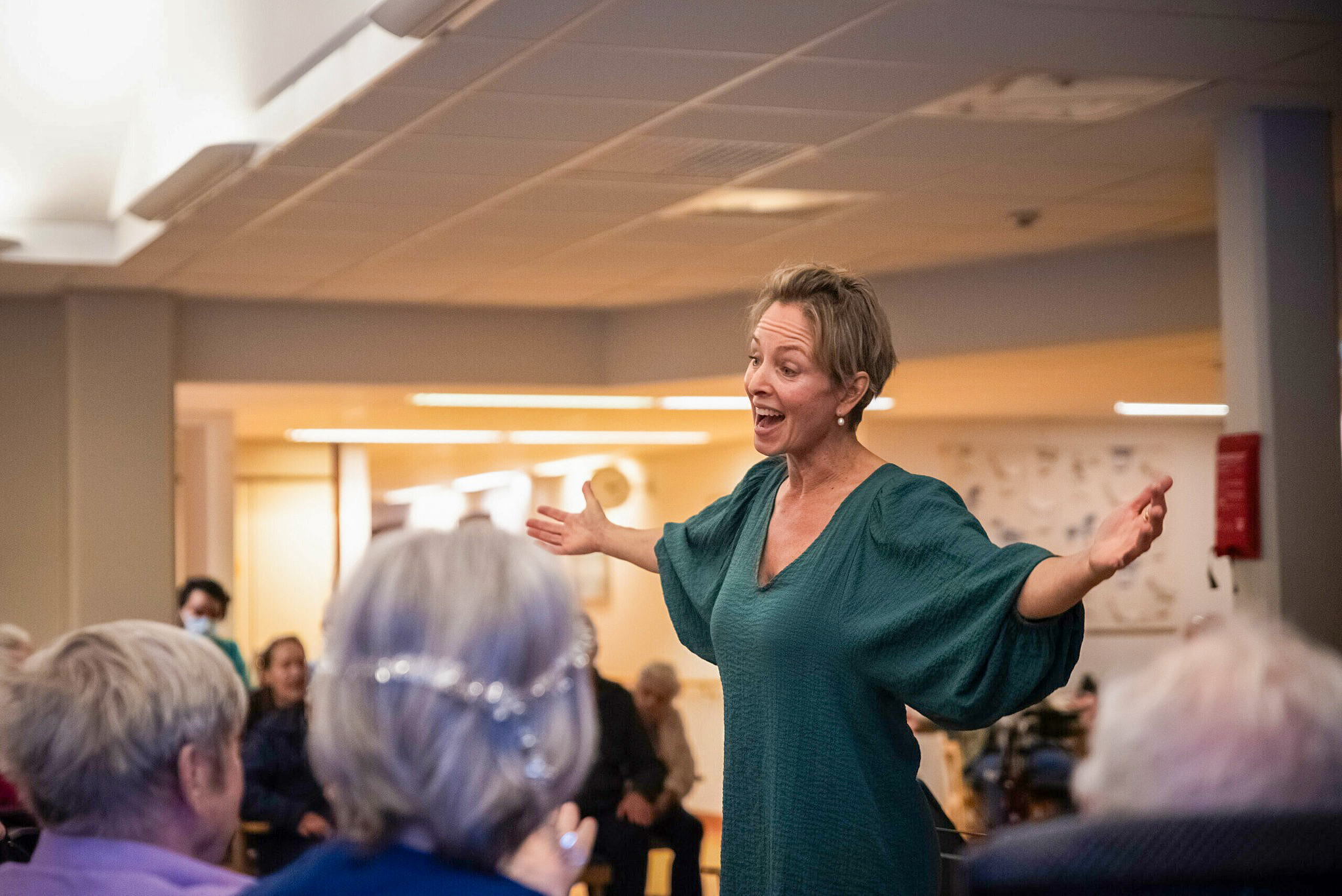 Kvinna med armarna utsträckta sjunger framför en publik.