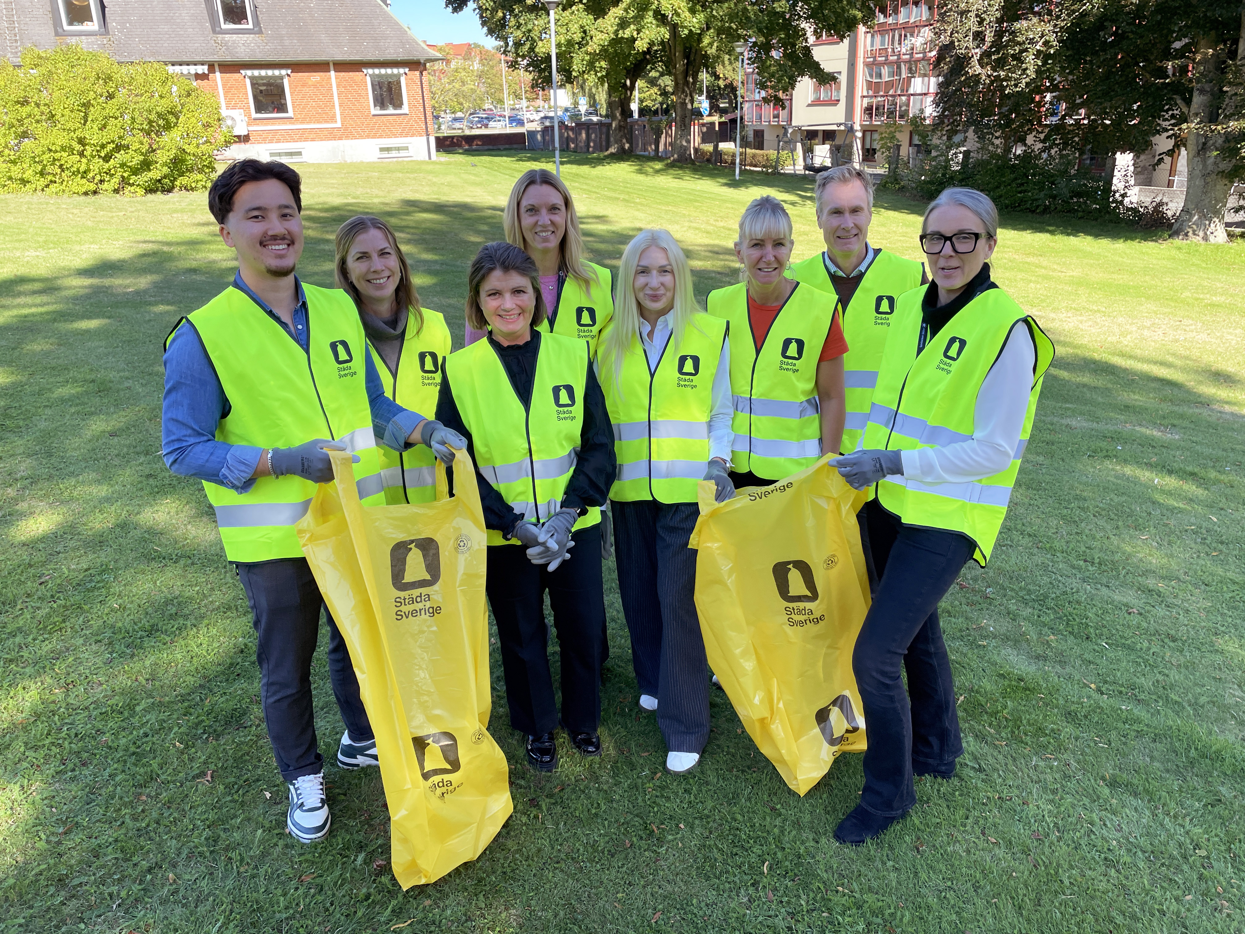 Åtta personer står tillsammans i gula västar och håller soppåsar.